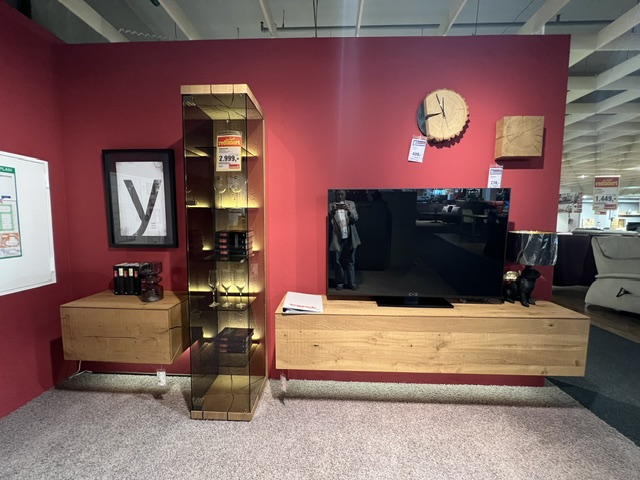 Wohnwand Vara aus Kerneiche, sägerau und gebürstet, mit TV-Möbel und Regal, auf rotem Hintergrund.