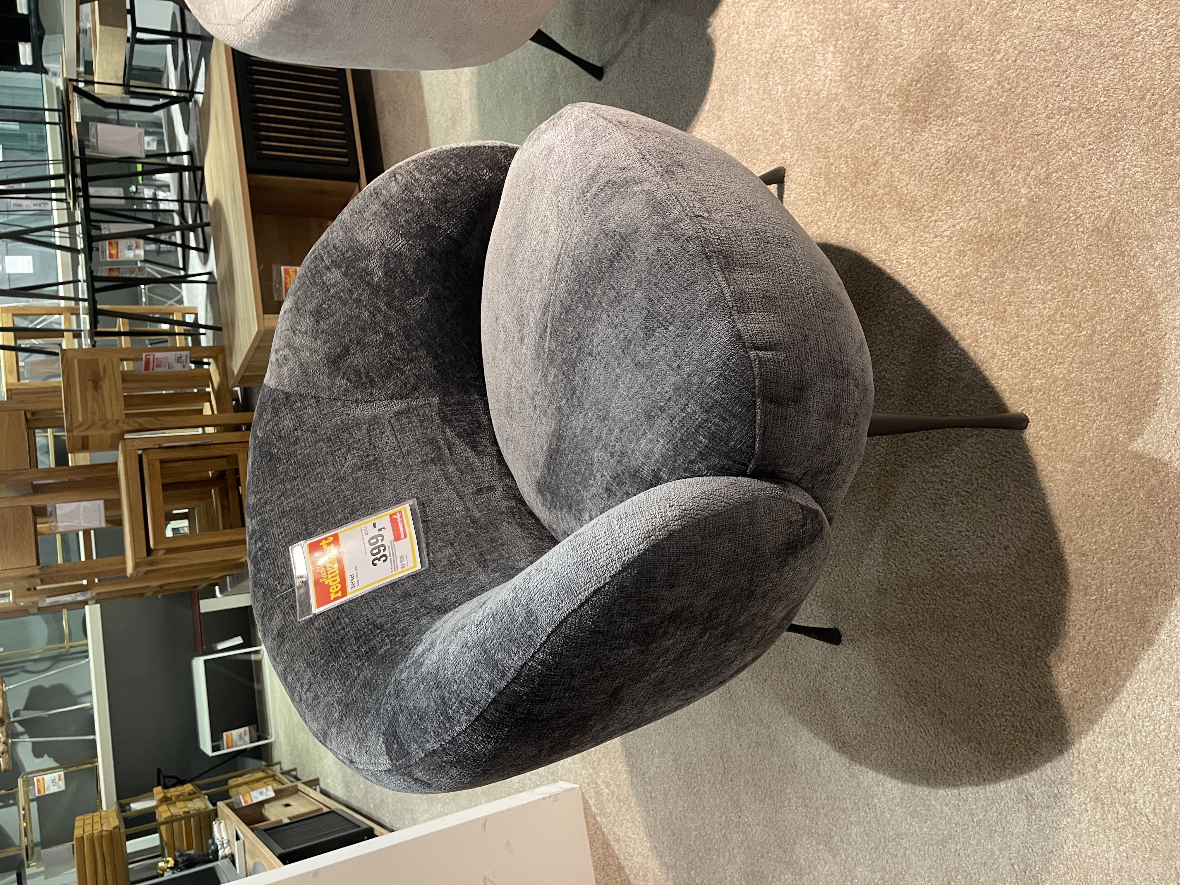 Grau gepolsterter Gutmann Sessel New Spirit mit runder Form und schwarzen Beinen.