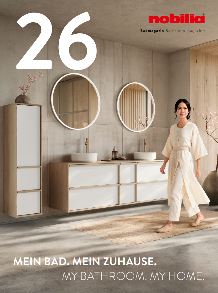 nobilia Badezimmer 2026 Modernes Badezimmer mit Holz- und weißen Möbeln, zwei runden Spiegeln und einer Person in einem Bademantel.