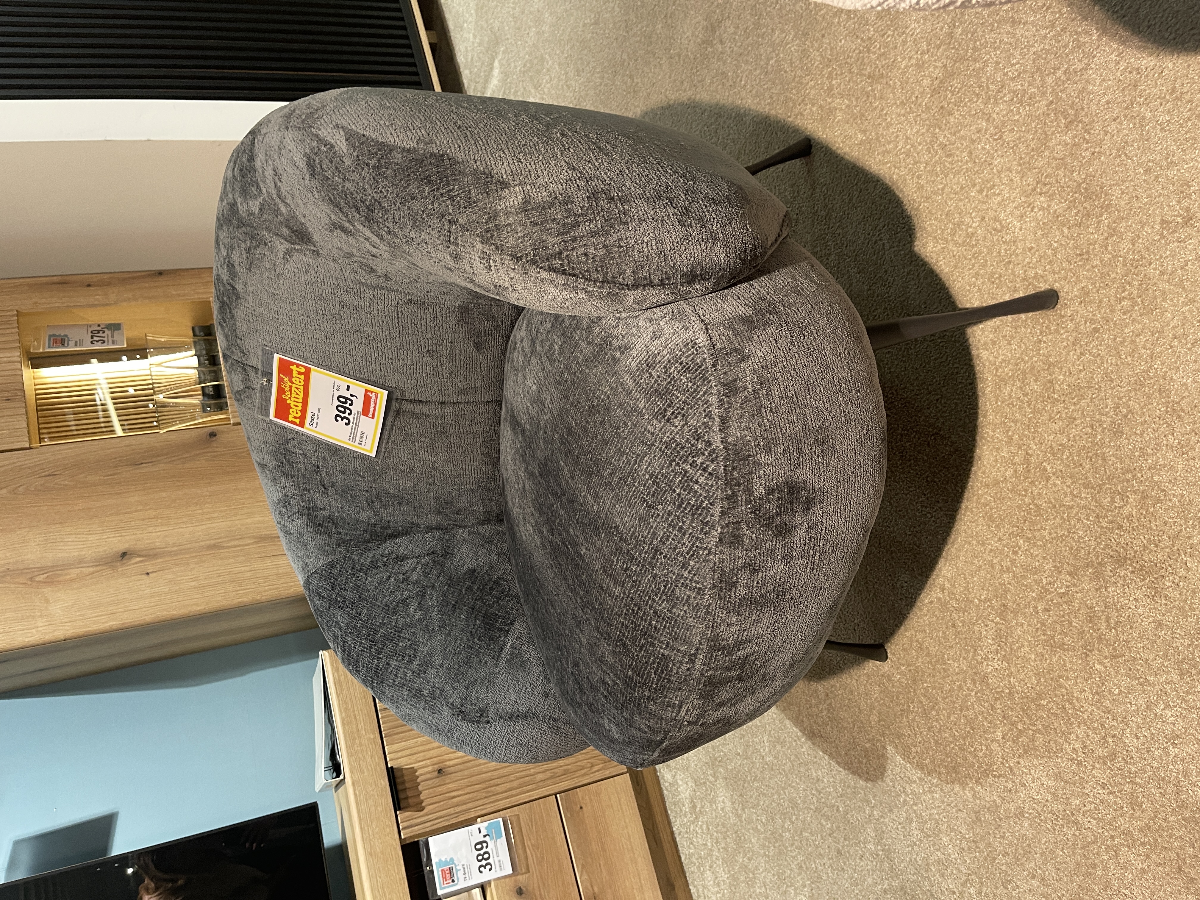 Grau gepolsterter Sessel "New Spirit" mit runder Form und schwarzen Metallbeinen.