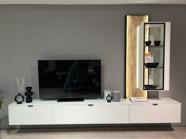 Wöstmann Wohnwand in Weiß mit TV-Element, Glaskasten und dekorativen Accessoires.