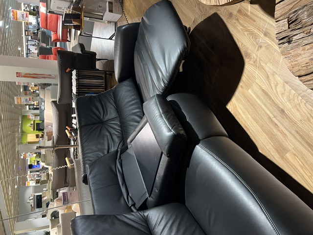 Trapezsofa mit zwei schwarzen Cumuly-Sesseln aus Leder und Ablage auf Holzfußboden.
