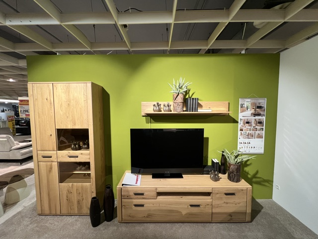 Wohnwand Alento aus Balkeneiche mit TV-Element, Regale und Vitrine, auf grünem Hintergrund.