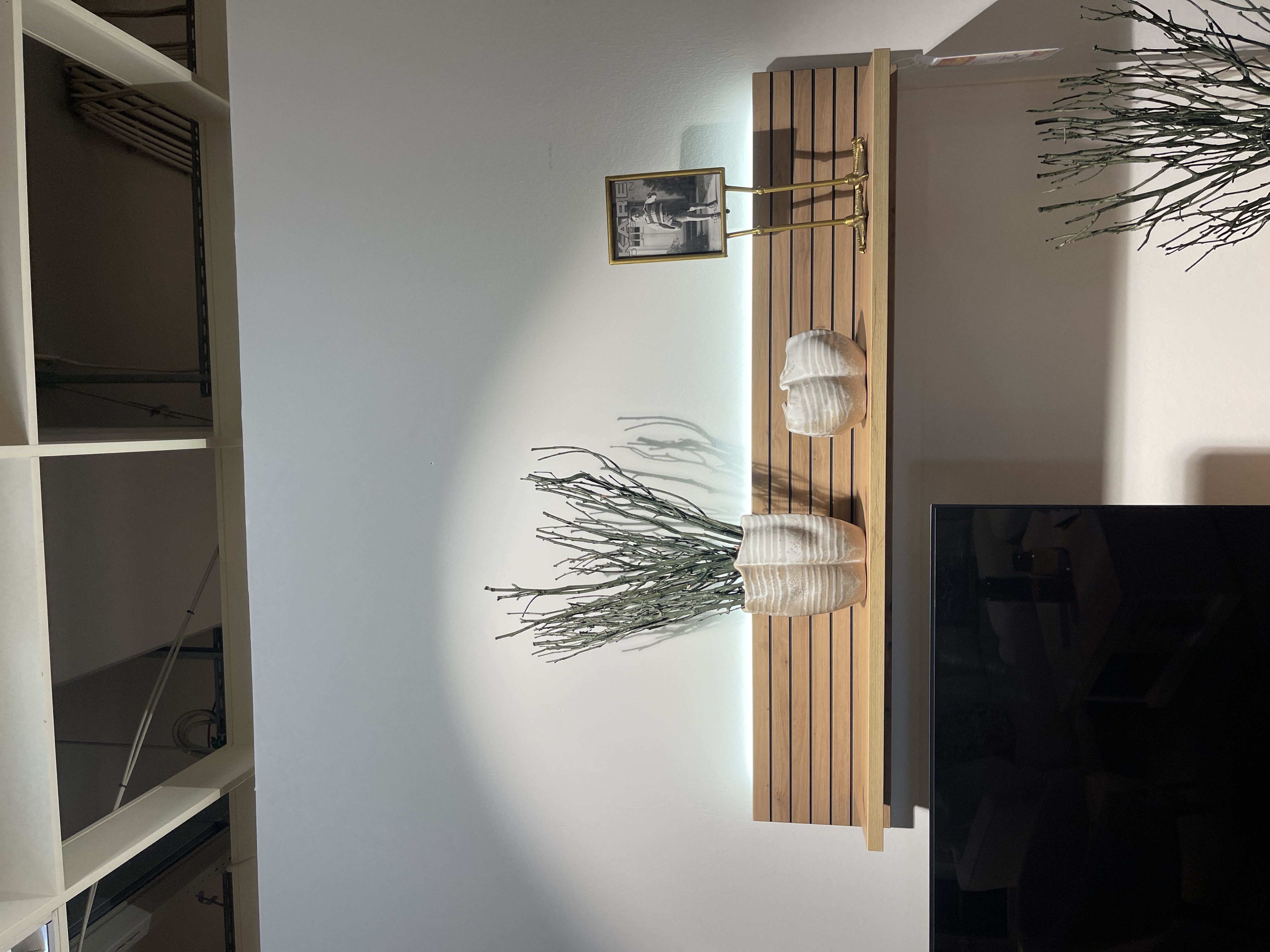Wandboard Core aus Artisan Eiche mit Rillenoptik und integrierter Beleuchtung, dekoriert mit Vasen und einem Bilderrahmen.