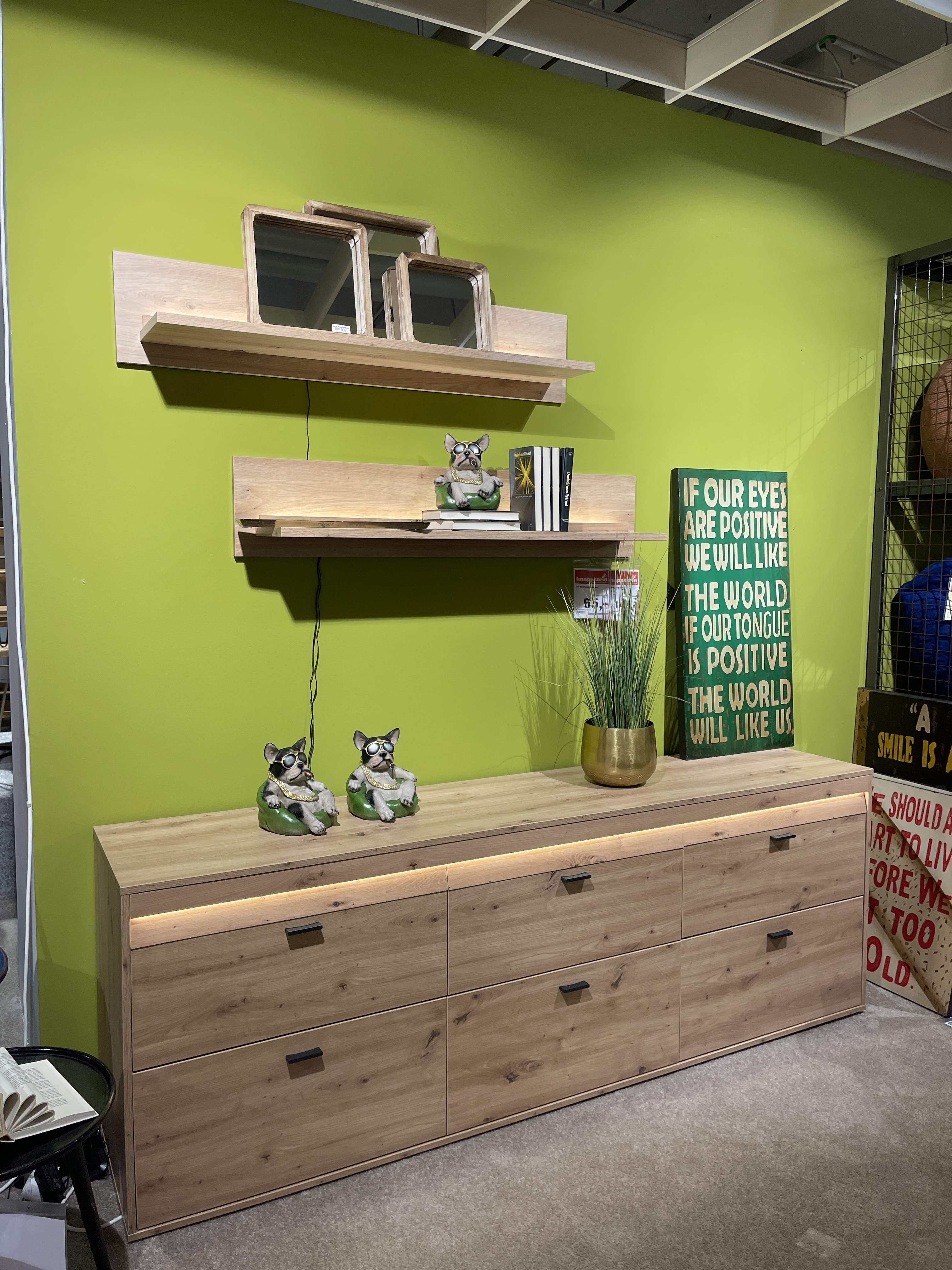Wohnwand Boca in Eiche Artisan Dekor mit Schubladen und Regalelementen, dekoriert mit Pflanzen und Figuren.